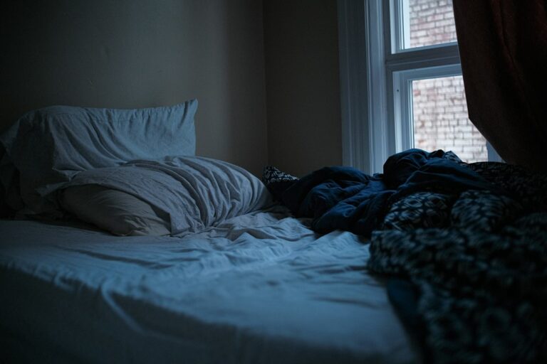 An unmade bed in a dark, quiet bedroom, ready for daytime sleep after a night shift.