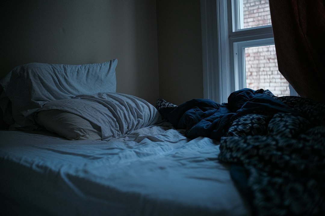 An unmade bed in a dark, quiet bedroom, ready for daytime sleep after a night shift.